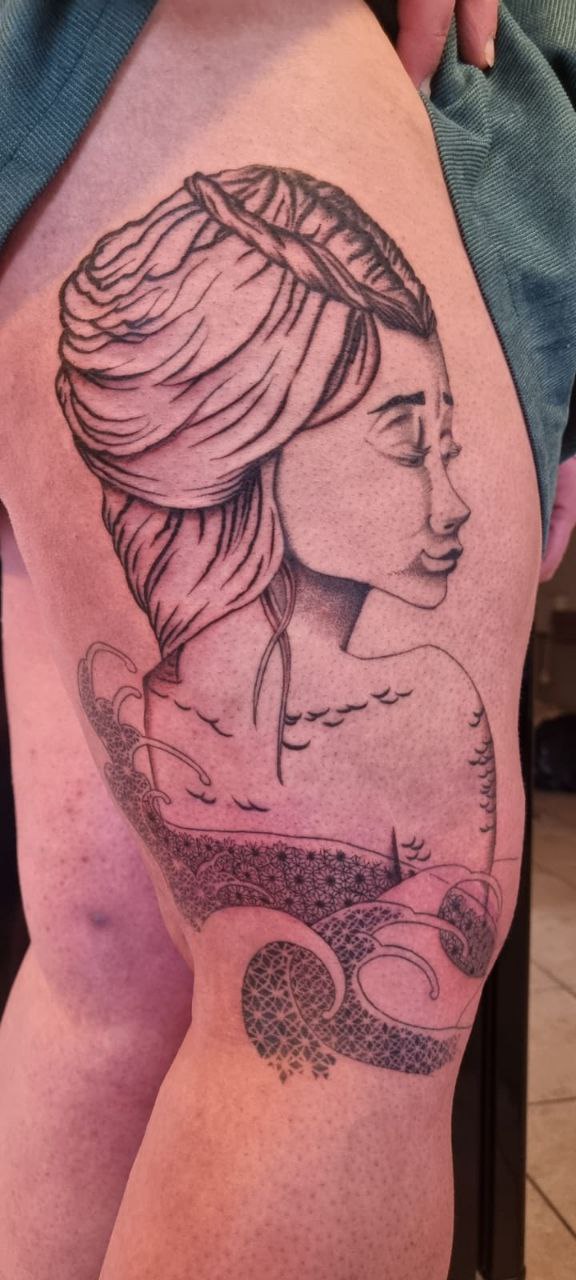 tatouage d'une déesse des eaux, un grand visage de femme aux air de possion semble sortir de vagues mistiques, finement ornementées.